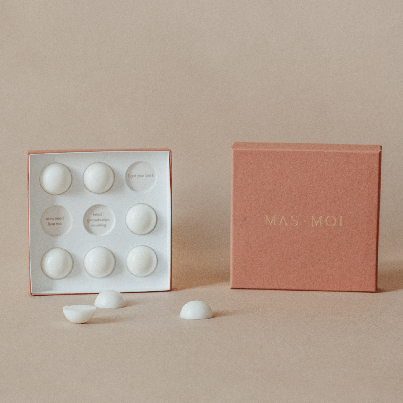 An open masmoi box revealing floral scent massage oil pearls inside, each designed to melt into nourishing oil for a soothing massage. The inner packaging includes playful text such as 'I got your back' and 'head goosebumps incoming,' adding a personalised touch. Set against a warm beige background, this luxurious product is perfect for a massage workshop or self-care ritual.